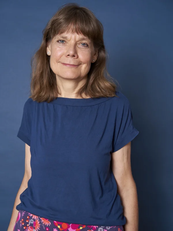 Foto unserer Bereichsleitung. Sie trägt ein blaues T-Shirt und einen bunten Rock und lächelt freundlich.