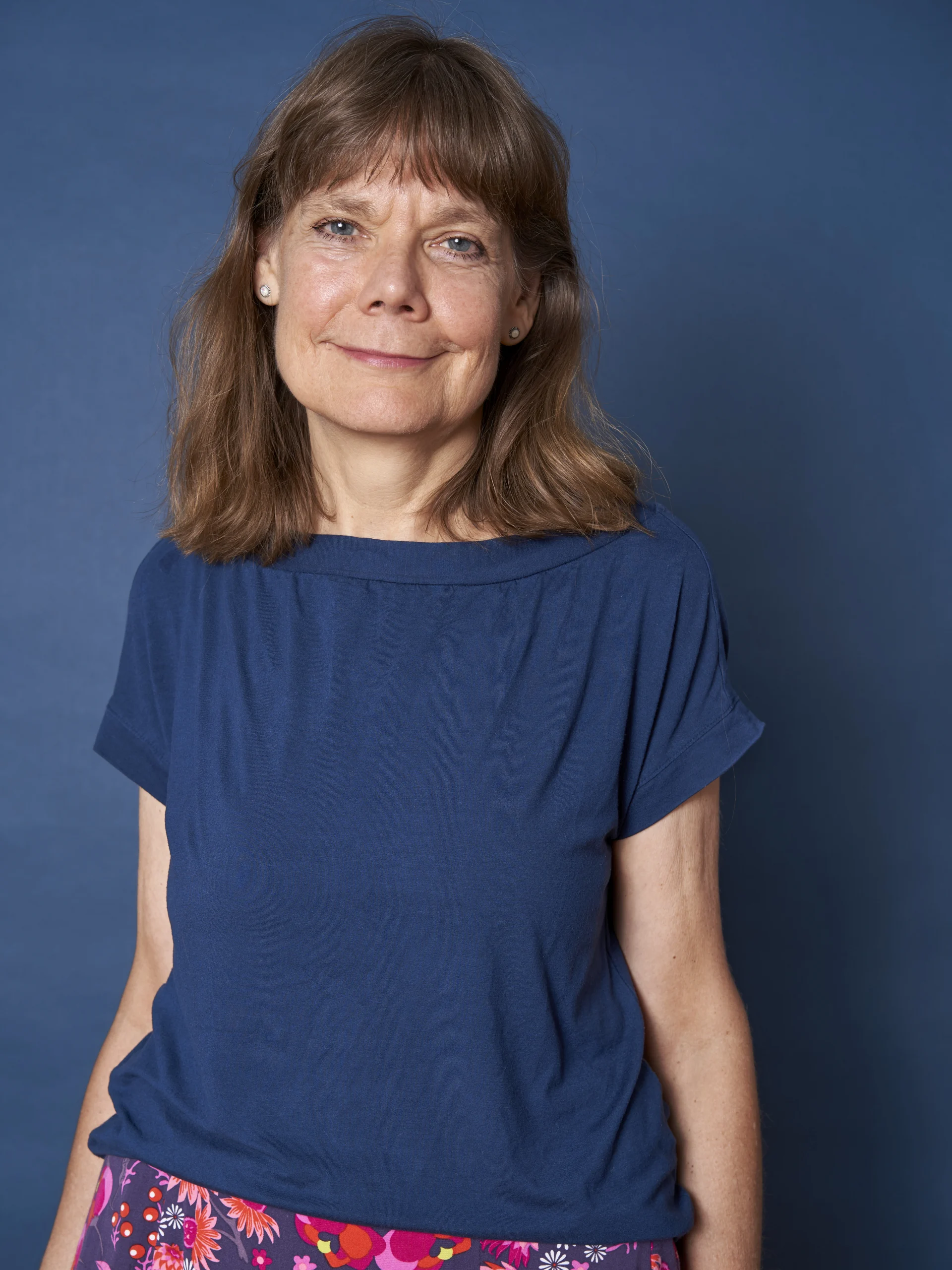 Foto unserer Bereichsleitung. Sie trägt ein blaues T-Shirt und einen bunten Rock und lächelt freundlich.