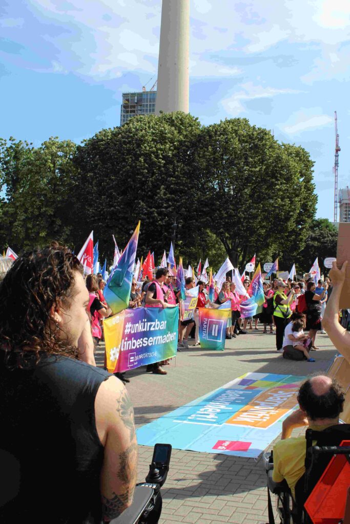 Jugendhilfe in Aktion: zahlreiche Angehörige der sozialen Berufe in Berlin heben Banner und Flaggen. Die bunten Farben der Transparente stehen unter anderem für den Wunsch nach einem vielfältigen und gerechten Sozialstaat.